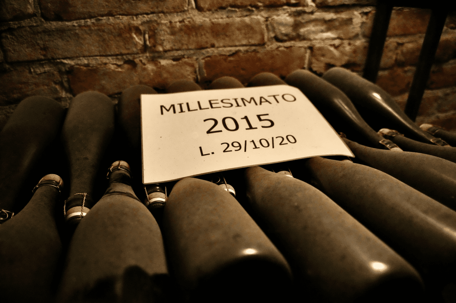 Vintage Italian sparkling wine bottles aging on lees in a brick cellar, labeled Millesimato 2015