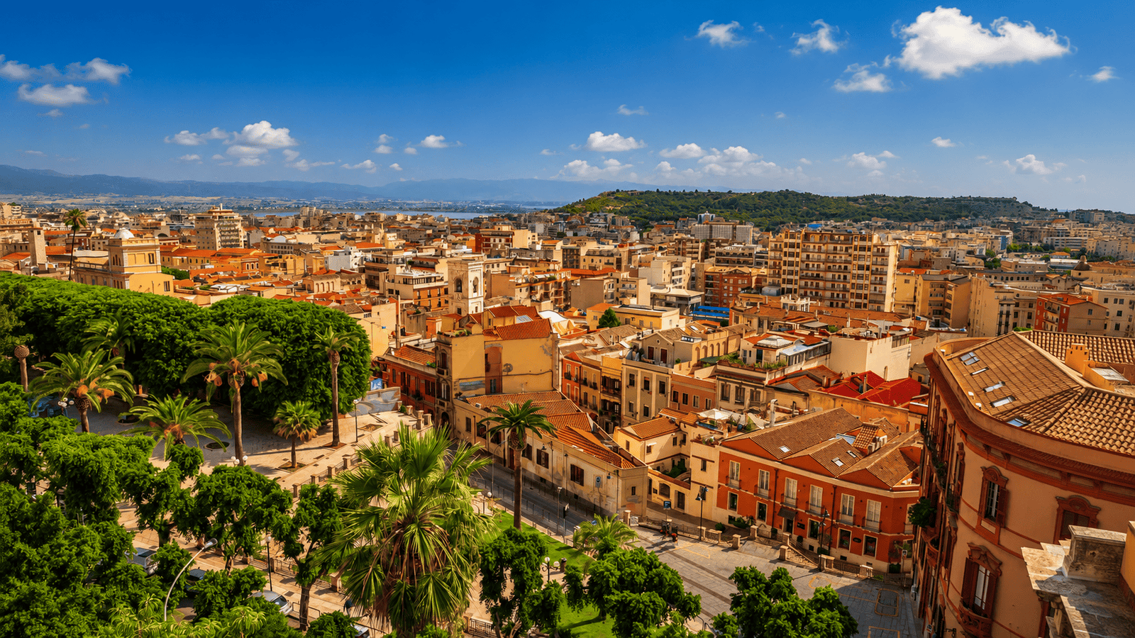 Panoramic view of Cagliari city and harbor in Sardinia on a sunny day with palm trees and colorful buildings.