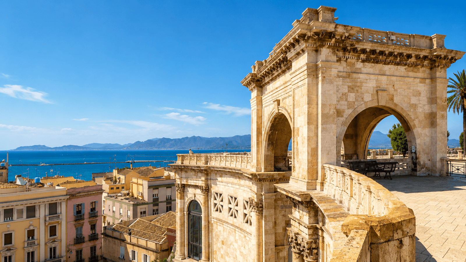 Cagliari, Sardinia: Ornate stone bastion overlooking a colorful city, a blue harbor, and distant mountains.