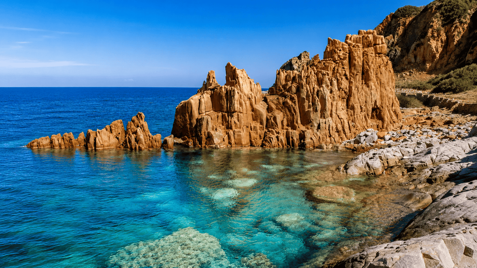 Dramatic red granite rock formations meet clear turquoise waters on Sardinia's sunny coastline.